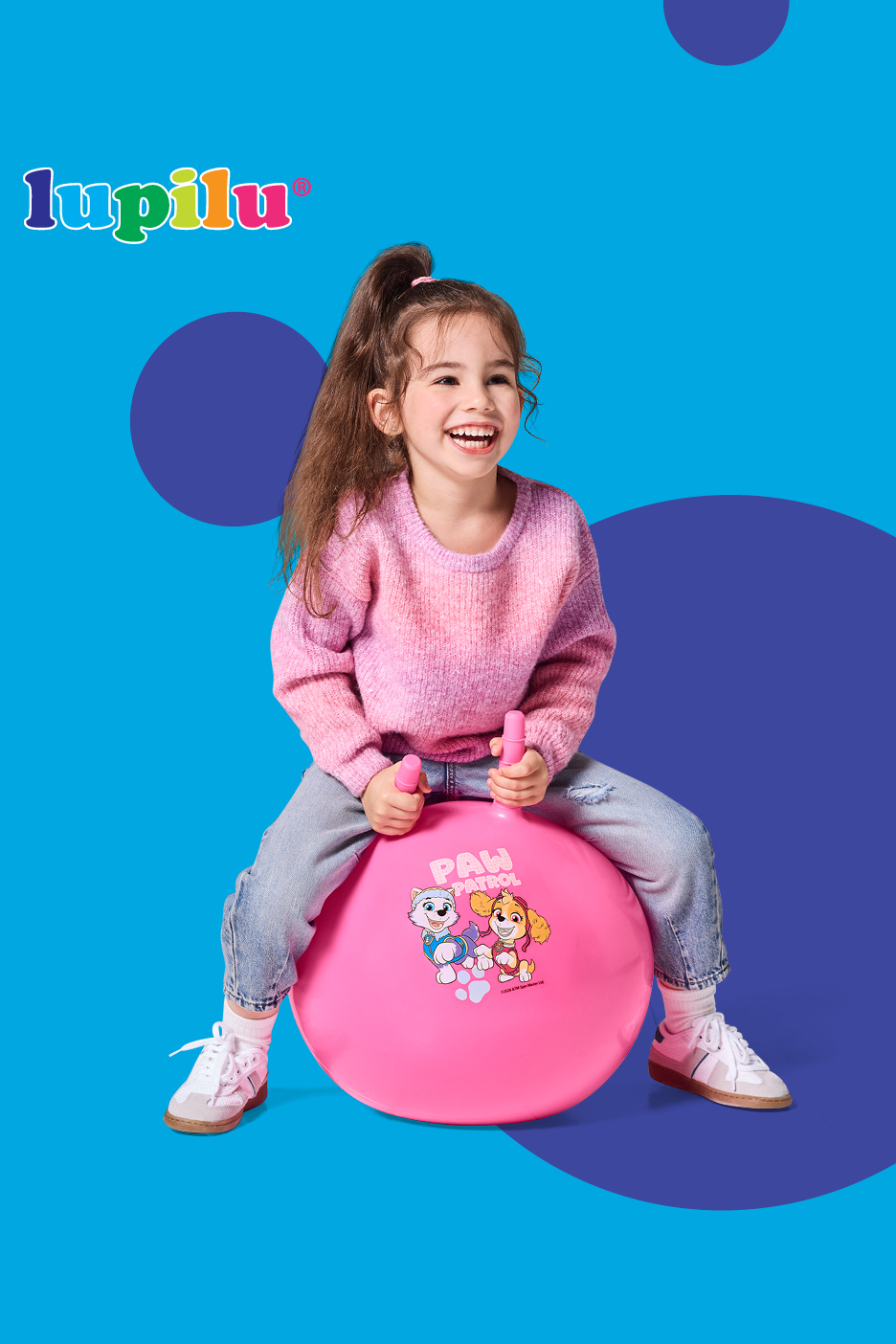 Deklica se smehlja na rožnati žogi za poskakovanje z motivi kužkov.