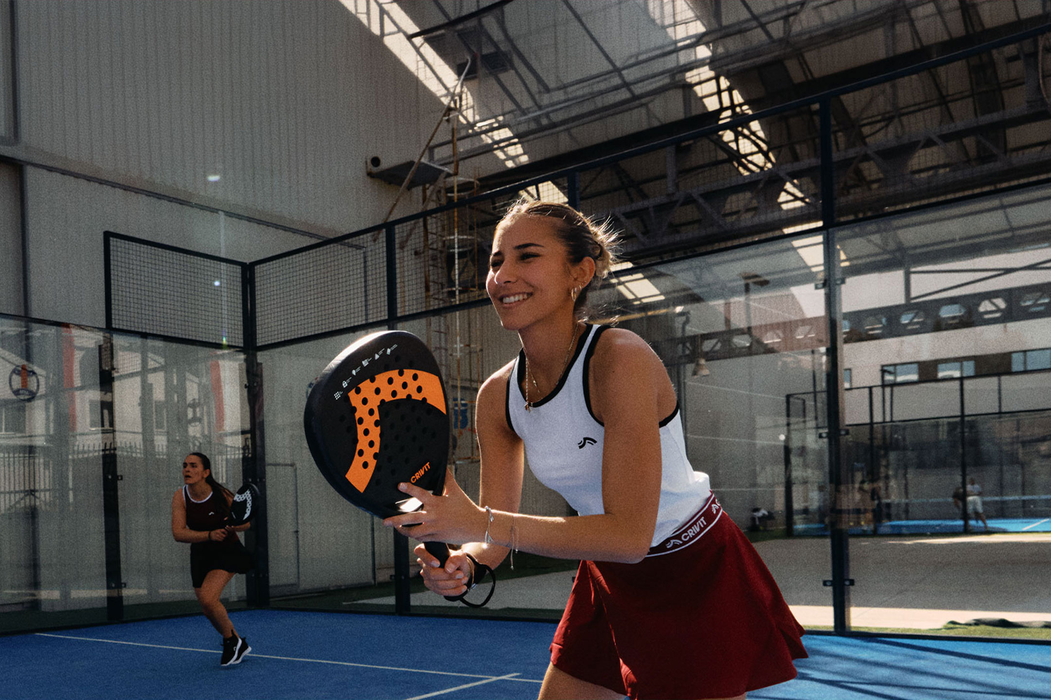 Ustvarjeno z umetno inteligenco: Dve ženski igrata padel tenis, ena se nasmiha in drži lopar, na modrem igrišču.
