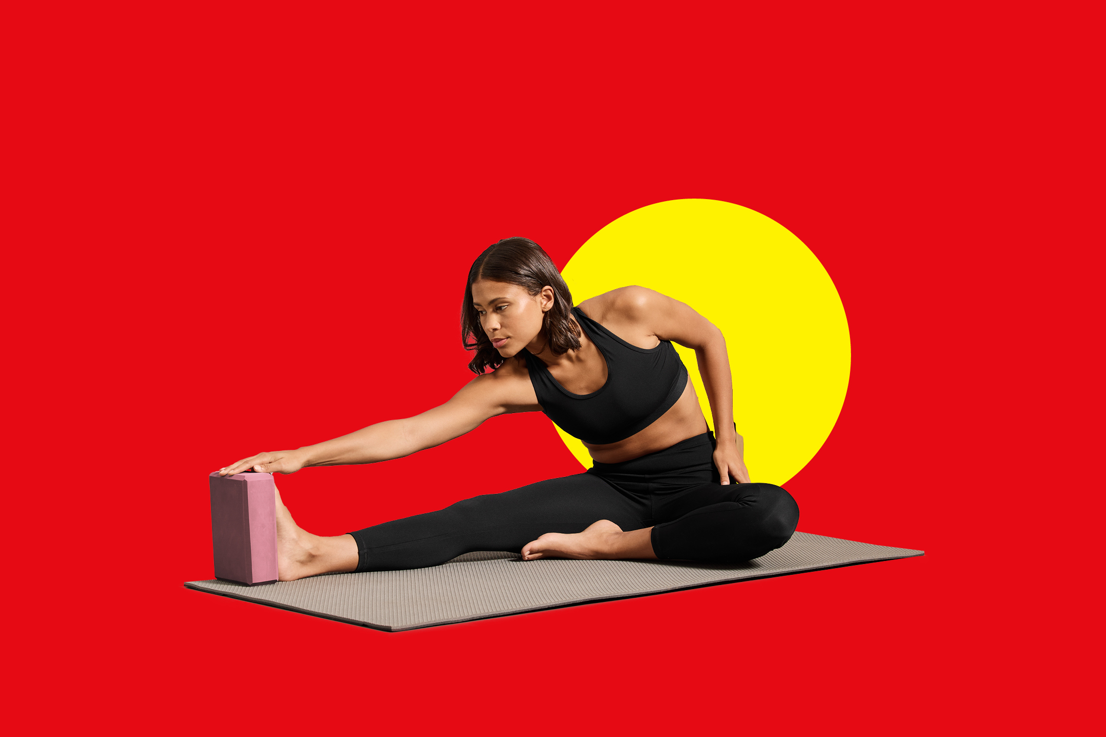 Ženska v črnih pajkicah in športnem modrčku se razteza z roko na rožnatem bloku za jogo.