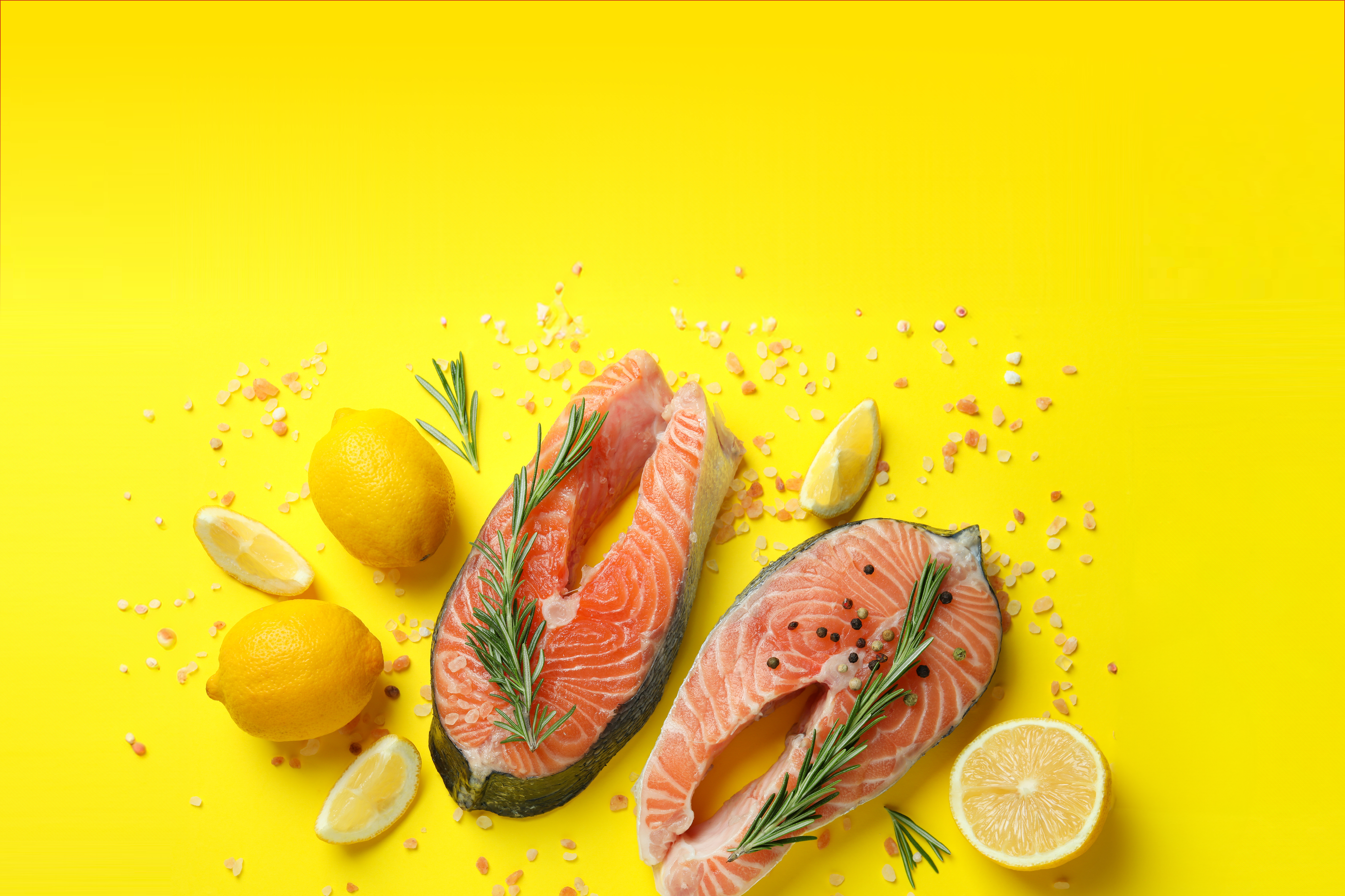 Dva lososova zrezka z limono, rožmarinom in soljo na rumeni podlagi.