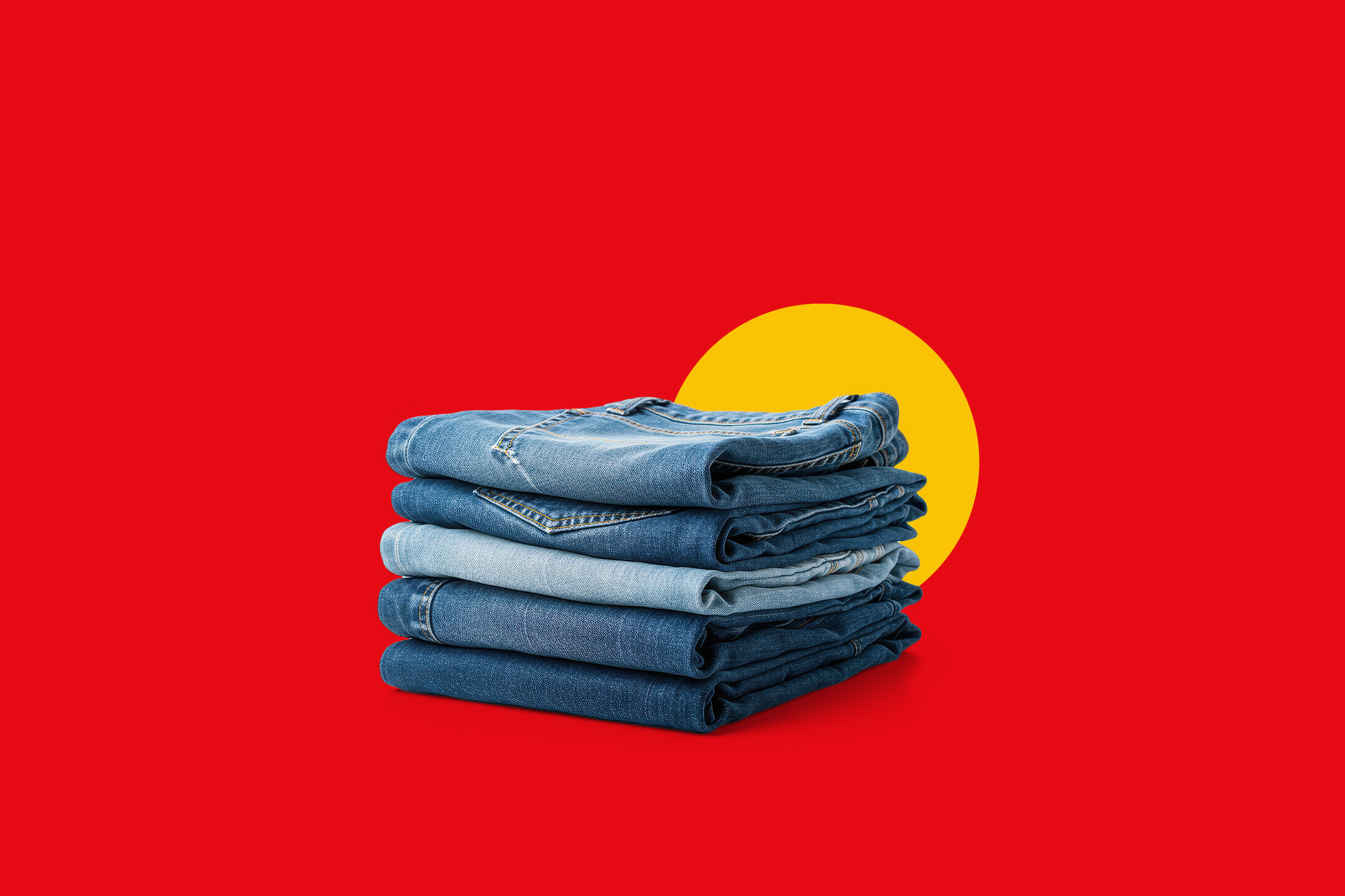 Kup zloženega jeansa v različnih odtenkih modre barve na rdečem ozadju z rumenim krogom.