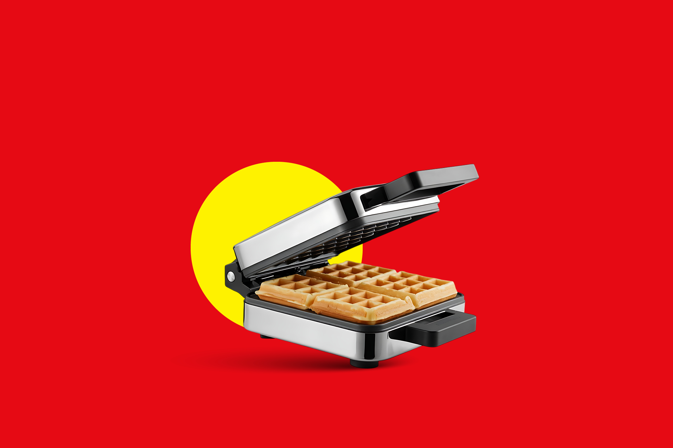 Odprt pekač za vaflje s štirimi pečenimi vaflji na rdečem ozadju z rumenim krogom.