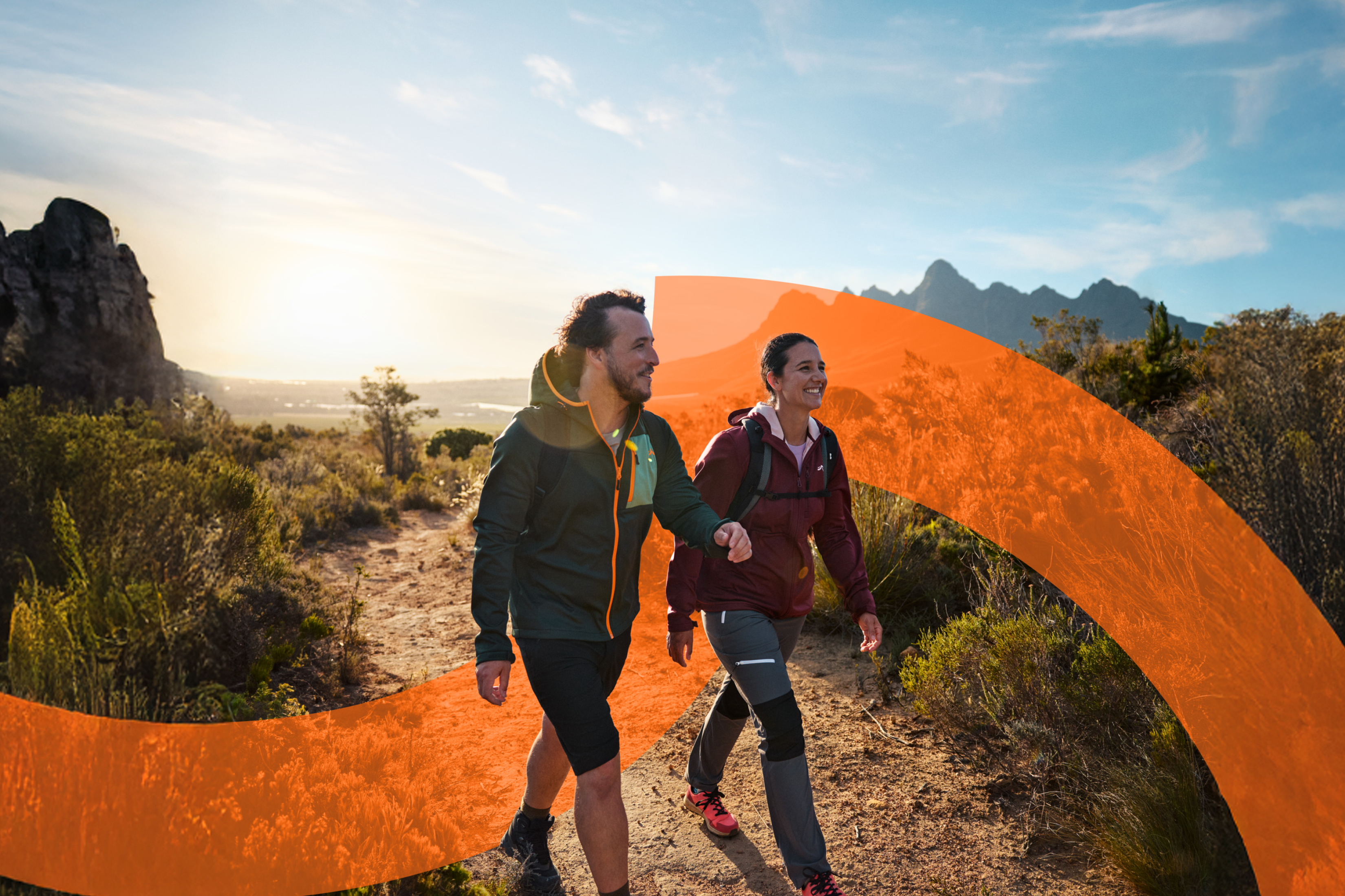 Par v pohodniških oblačilih in nahrbtnikih hodi po gorski poti ob sončnem zahodu.