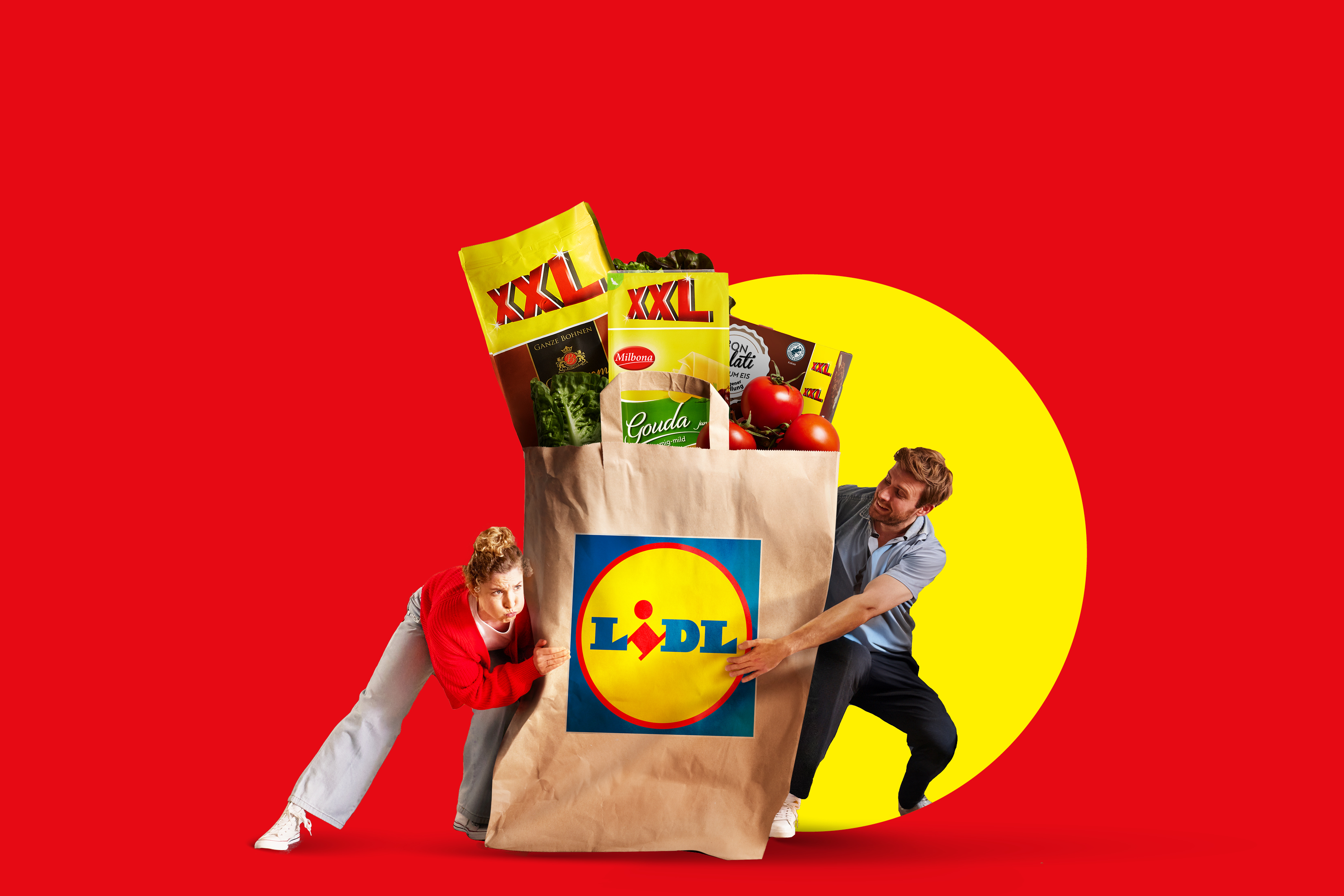 Moški in ženska se borita z veliko nakupovalno vrečko Lidl, polno izdelkov XXL, kot so sir Gouda, kava in solata.