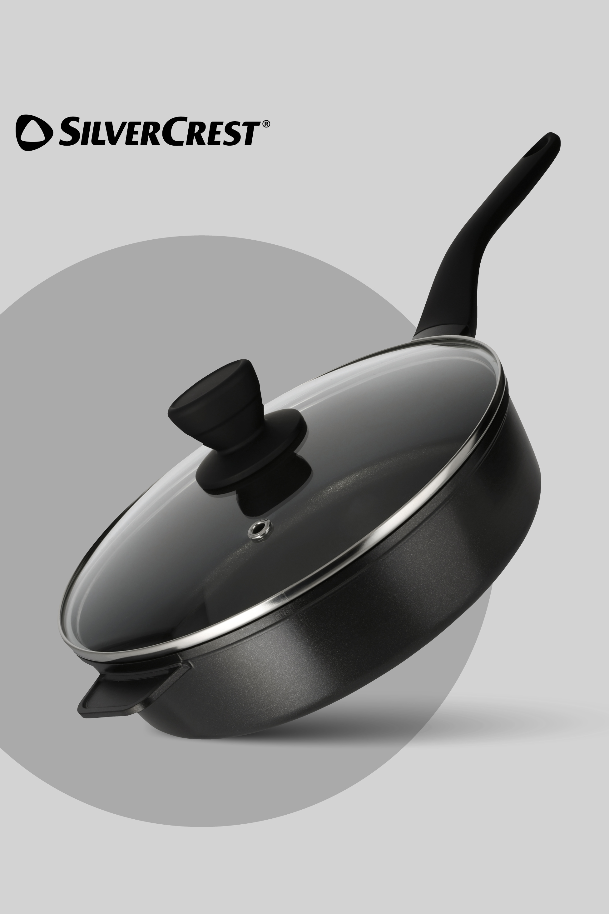 Črna ponev s pokrovom iz stekla in ročajem, ki stoji na sivi podlagi.