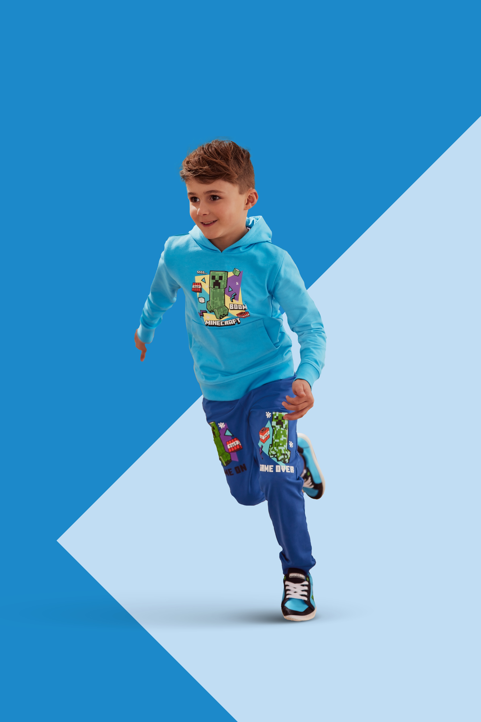 Deček v modri jopici s kapuco in hlačah s potiskom video igre.