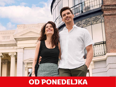 Par stoji pred staro stavbo, ona nosi črno majico in pikčasto krilo, on pa belo srajco in hlače.