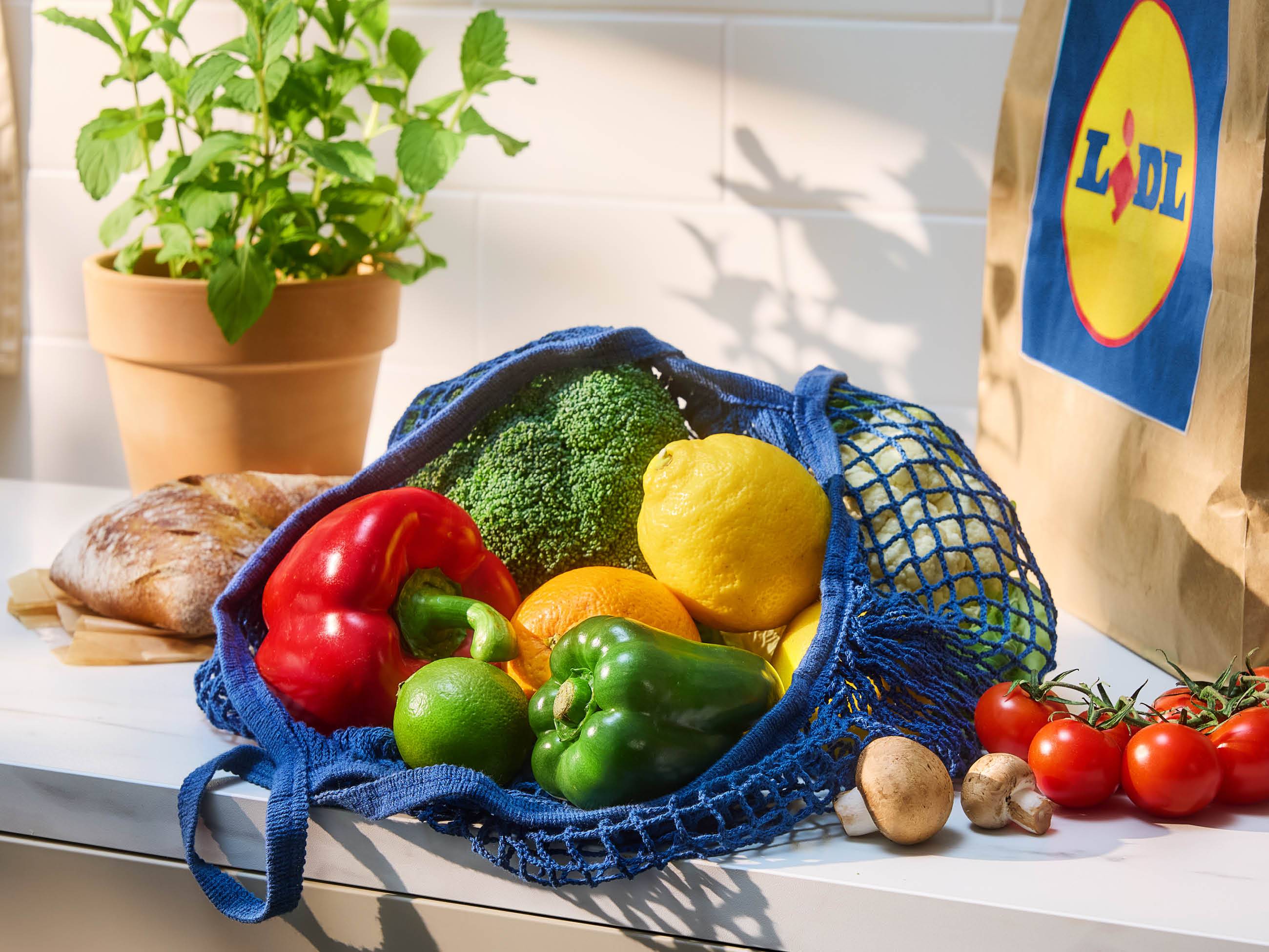 Sveže sadje in zelenjava v modri mrežici na pultu, poleg pa Lidl vrečka.