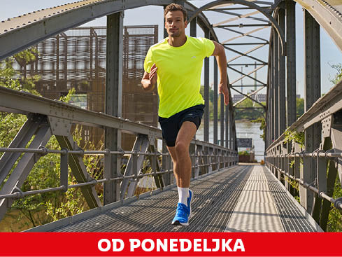 Moški tekač v svetlo rumeni majici in modrih supergah teče čez most.