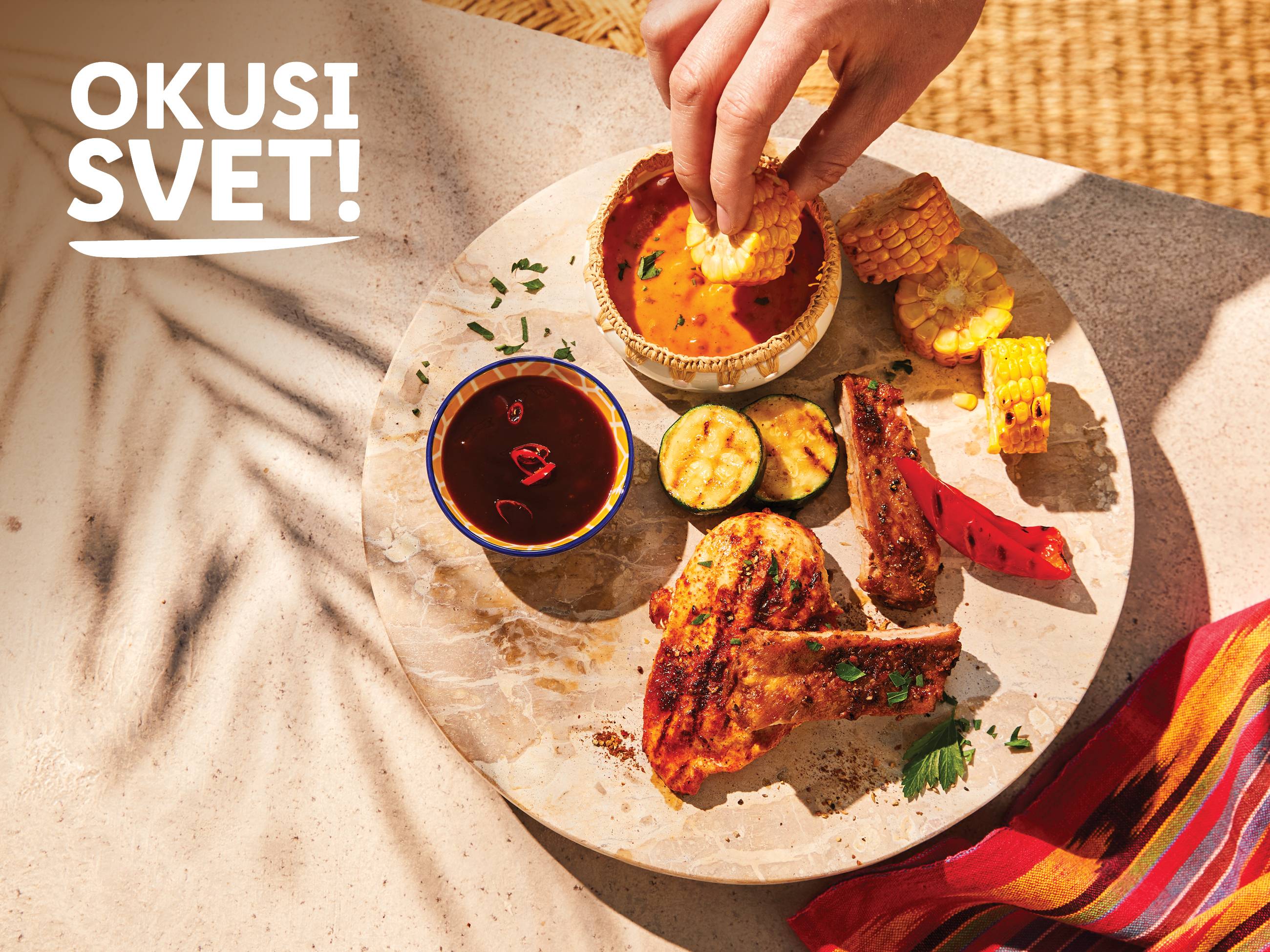 Pekač z žarom, vključno s piščancem, rebri, koruzo in omakami, z napisom »OKUSI SVET!«