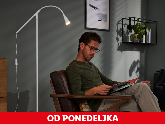 Moški bere v naslanjaču ob beli talni svetilki.