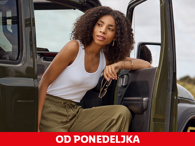 Ženska v belem topu in zelenih hlačah izstopa iz avtomobila.