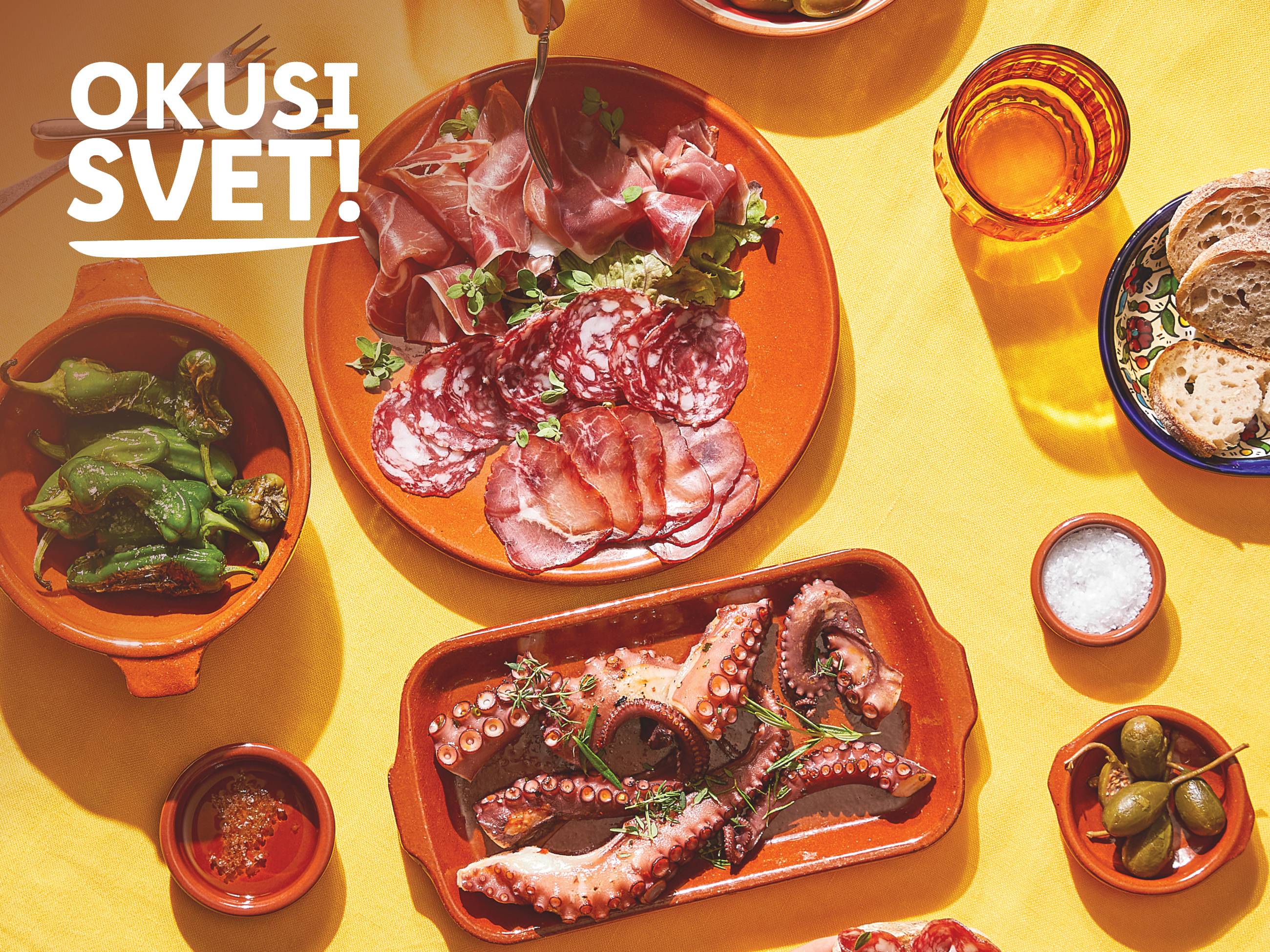 Španske tapasi s hobotnico, papriko, suhomesnatimi izdelki in kruhom na rumeni podlagi.