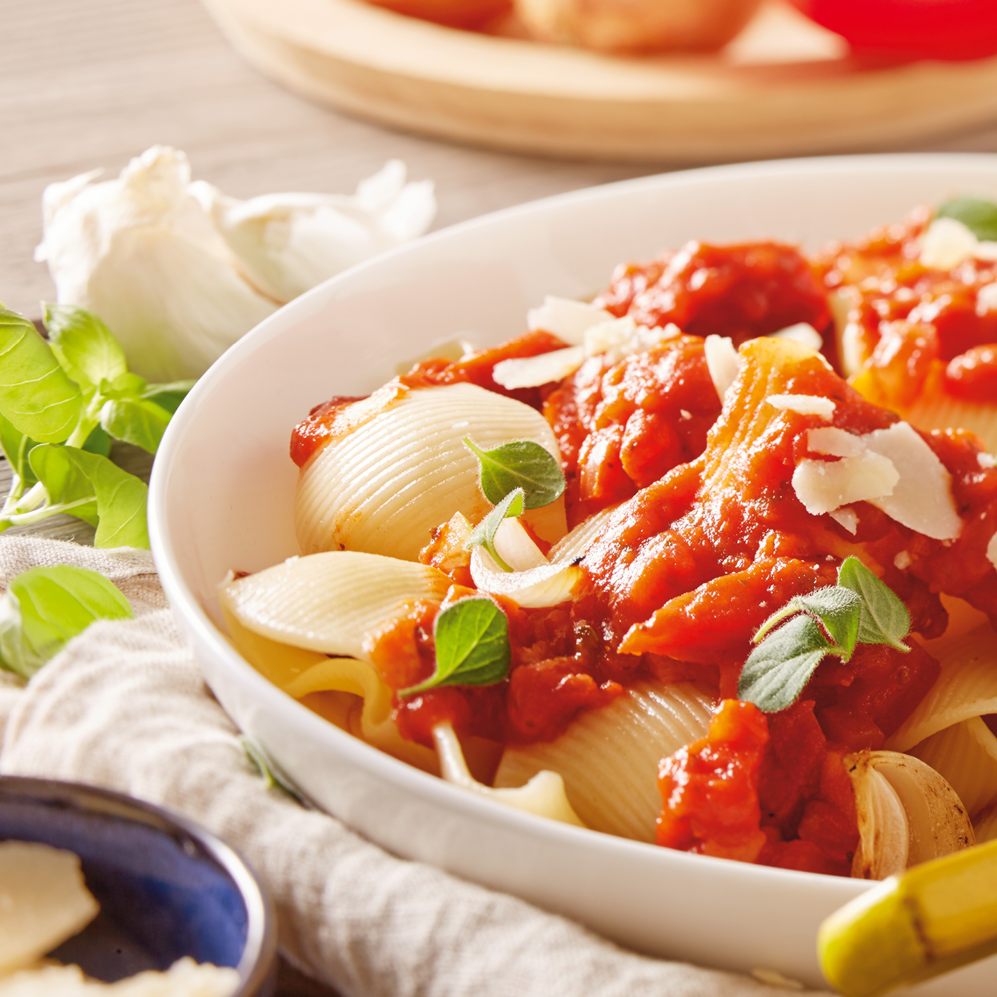 Krožnik testenin conchiglie z rdečo omako, sirom in zelišči.