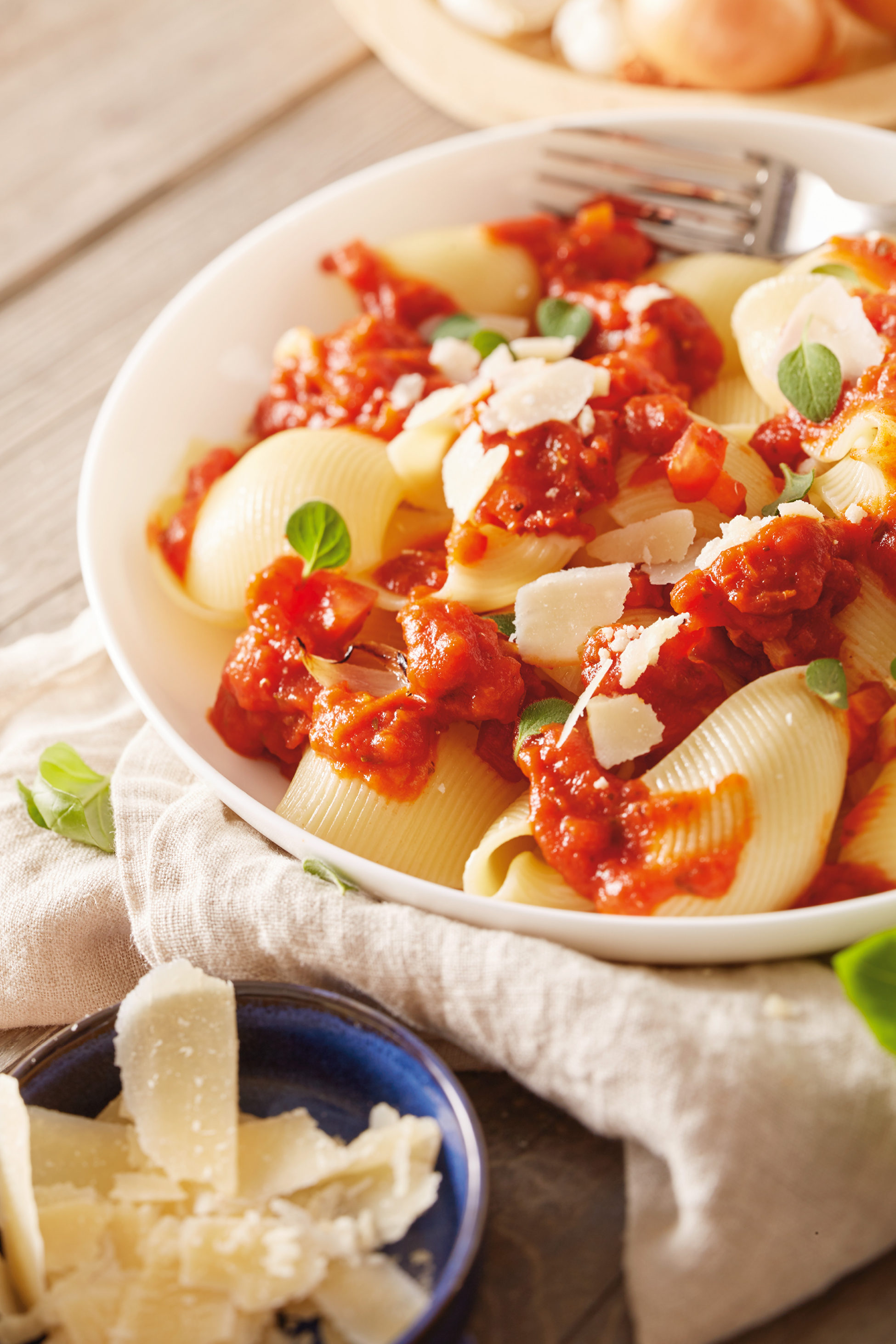 Skleda testenin conchiglie z rdečo omako, parmezanom in svežimi zelišči.