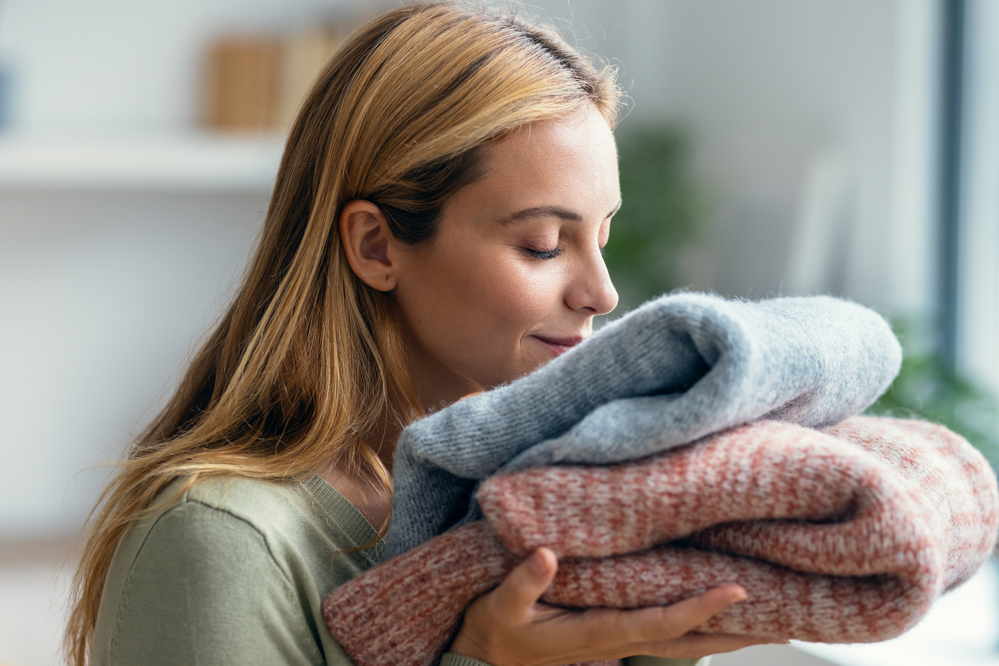 Ženska diši sveže oprana oblačila, zložene puloverje v rokah.