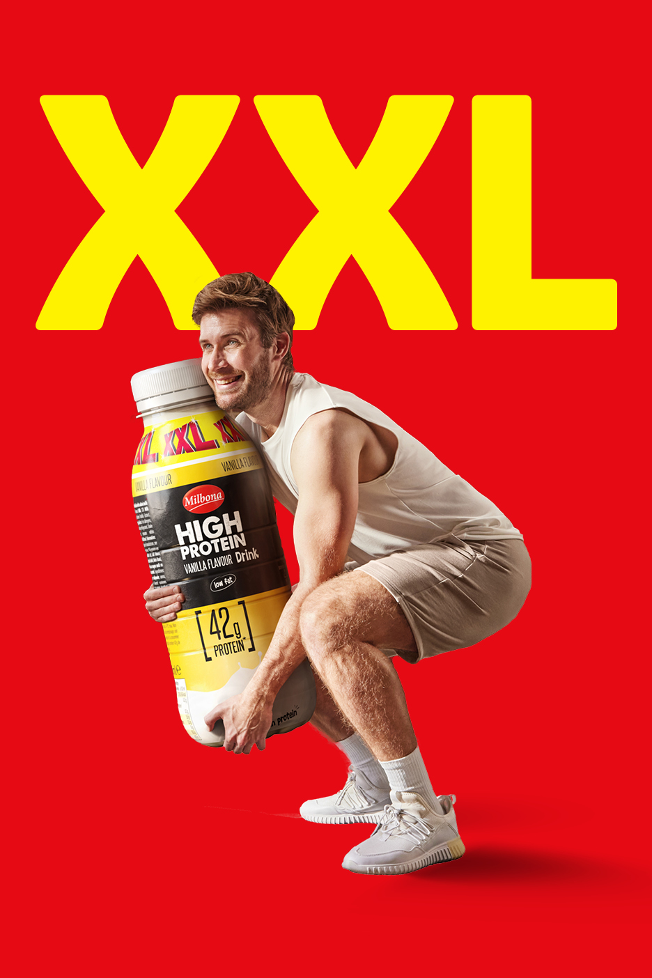 Moški v počepu drži ogromen beljakovinski napitek z okusom vanilije na rdečem ozadju z napisom XXL.