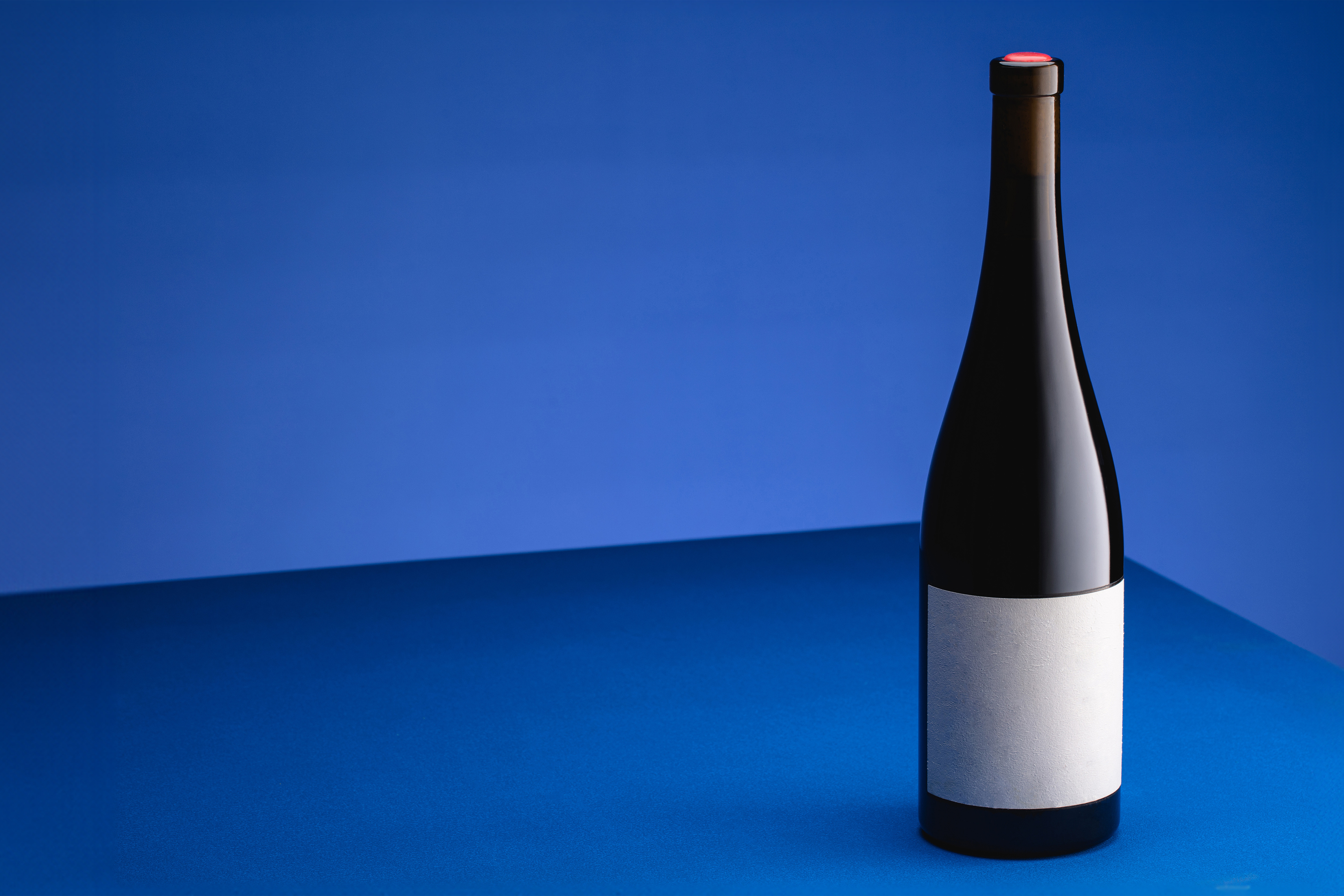 Steklenica rdečega vina z belo etiketo na modrem ozadju.