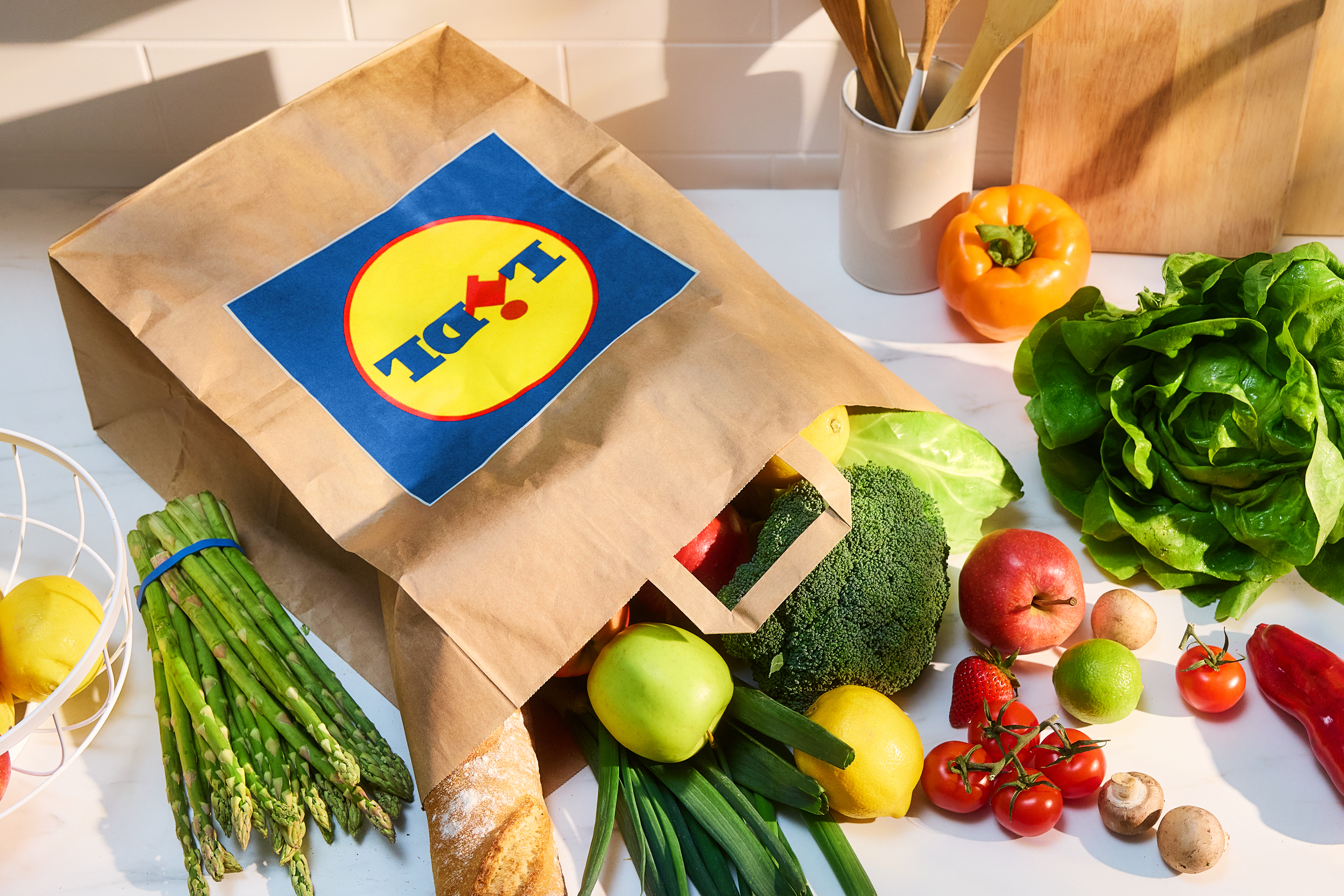 Lidl papirnata nakupovalna vrečka, polna svežega sadja in zelenjave na kuhinjskem pultu.