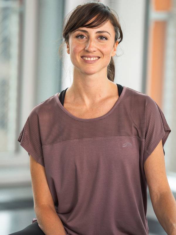 Nasmejana ženska v kratki vijolični športni majici.