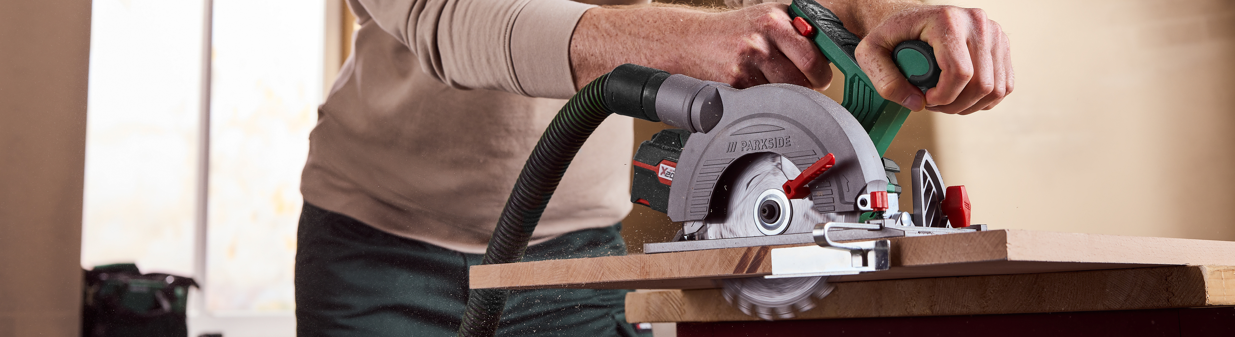 Moški reže les z ročno krožno žago, ki je priključena na cev za odsesavanje prahu.