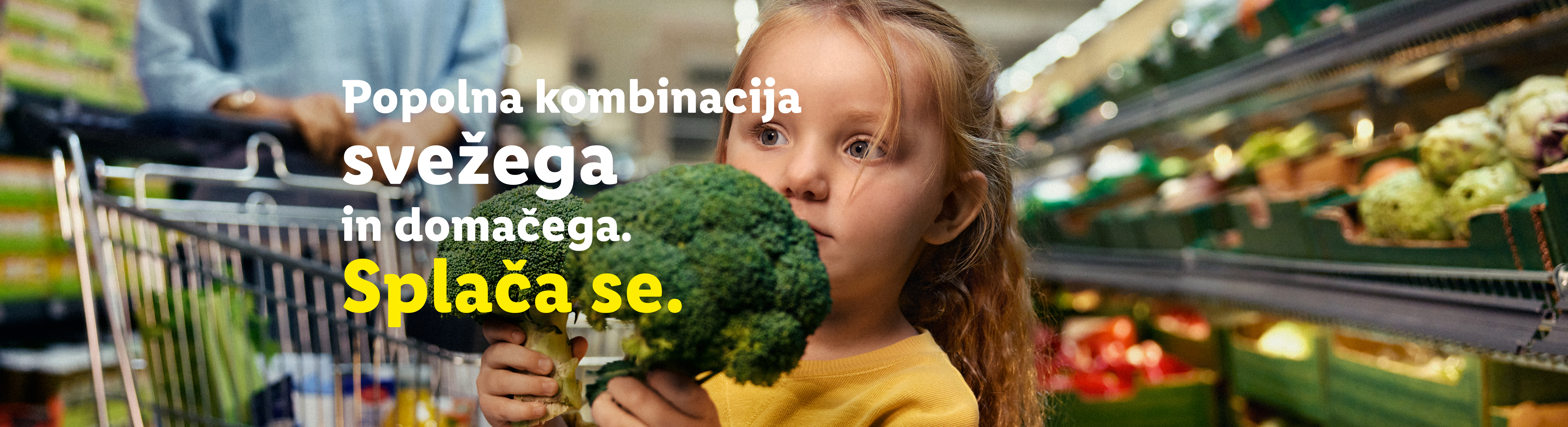 Deklica drži brokoli v supermarketu, z napisom o sveži in domači hrani.