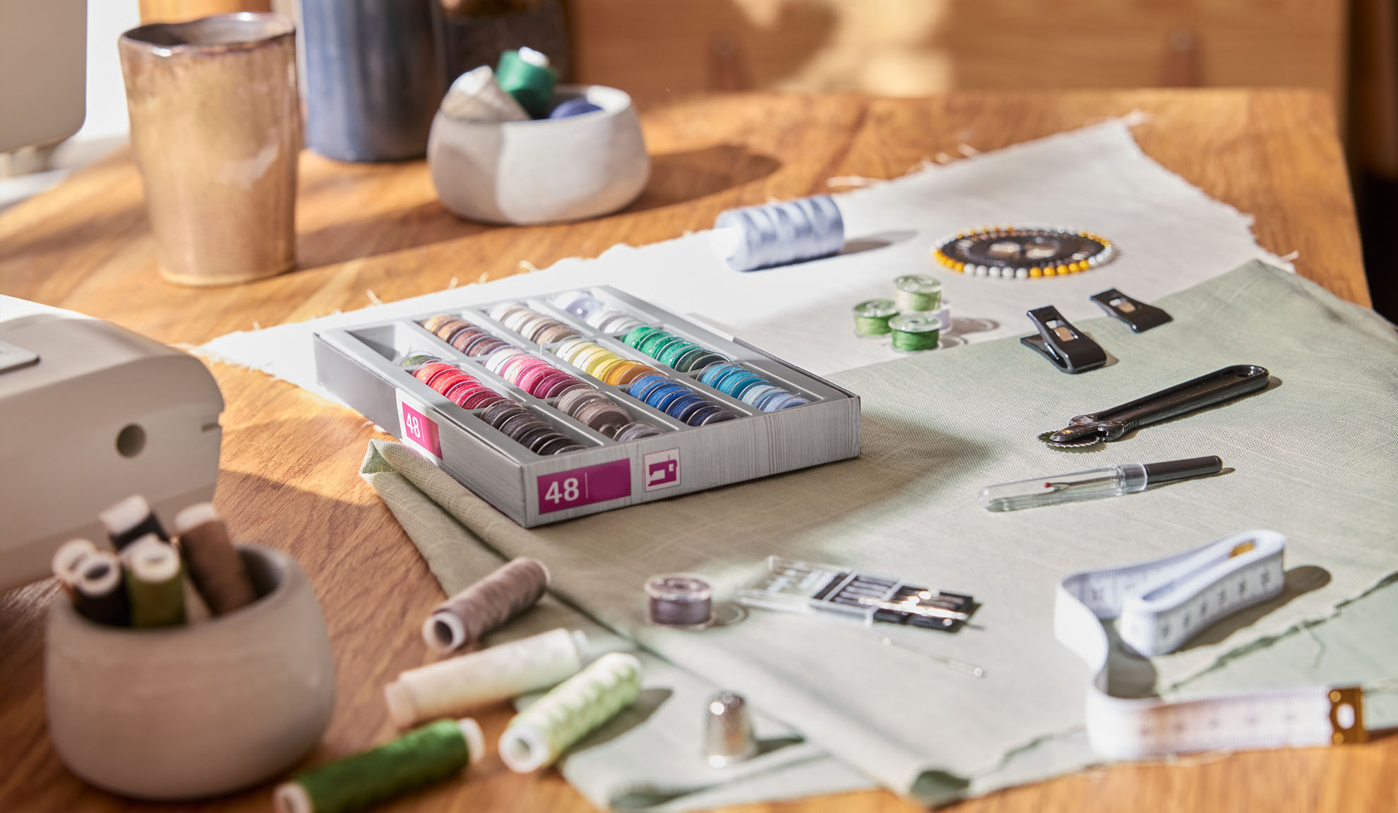 Šivalni komplet s škatlo barvnih niti, šivalnim strojem in različnimi orodji na leseni mizi.