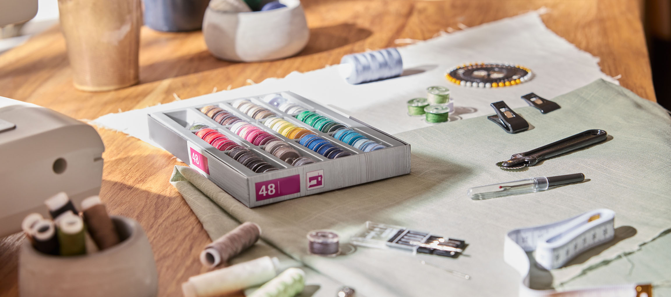 Šiviljski pripomočki na leseni mizi, vključno z organizatorjem sukancev z 48 navitji, tkanino in različnimi orodji.