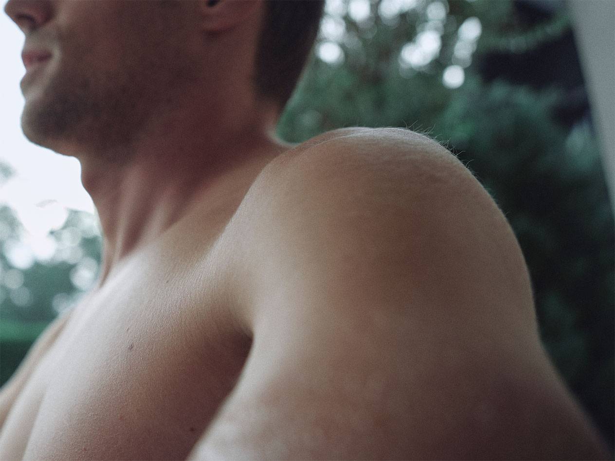 Povečava moškega ramena in vratu, z zamegljenim zelenim ozadjem.