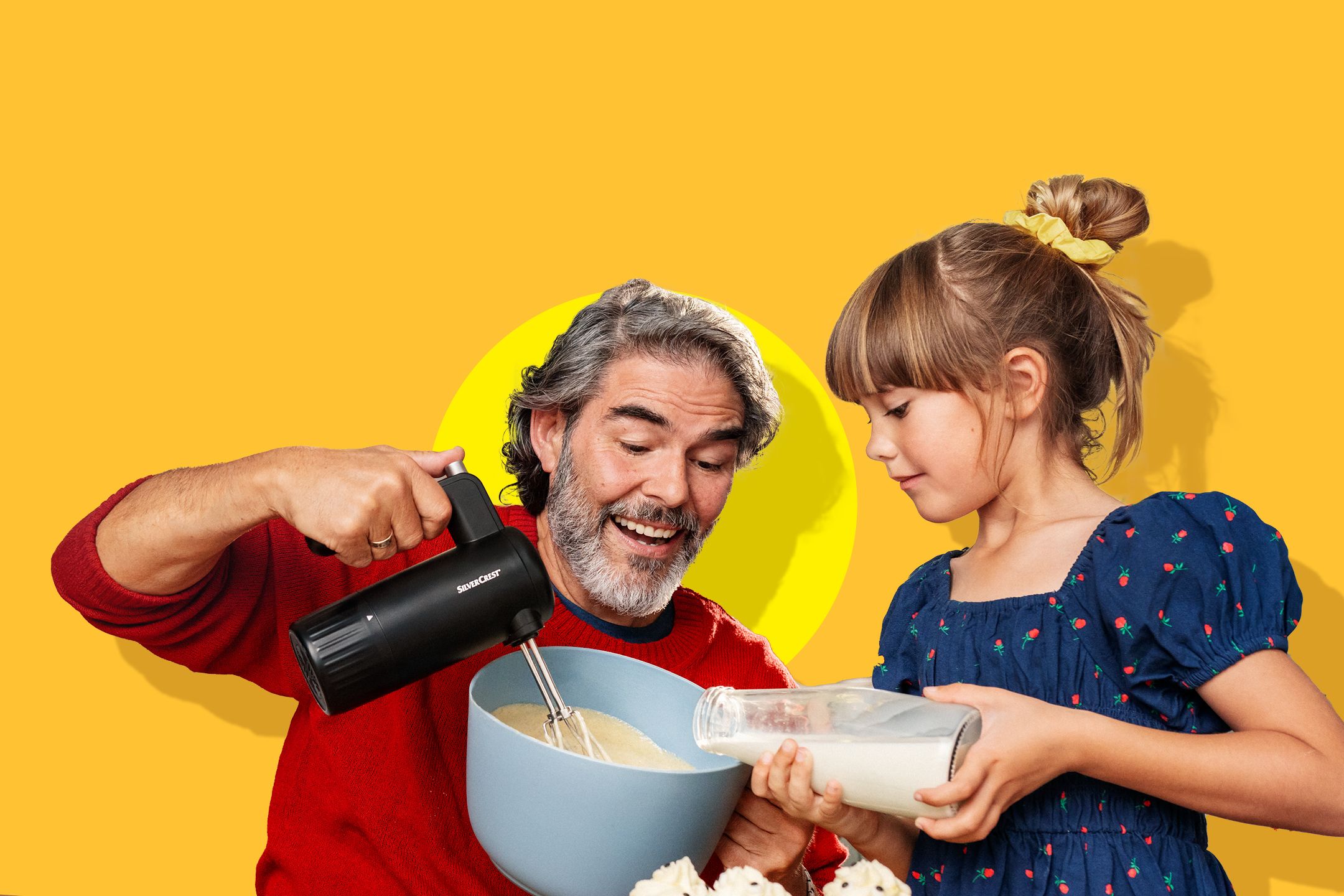 Oče in hči pečeta, uporabljata ročni mešalnik in vlivata mleko v skledo.