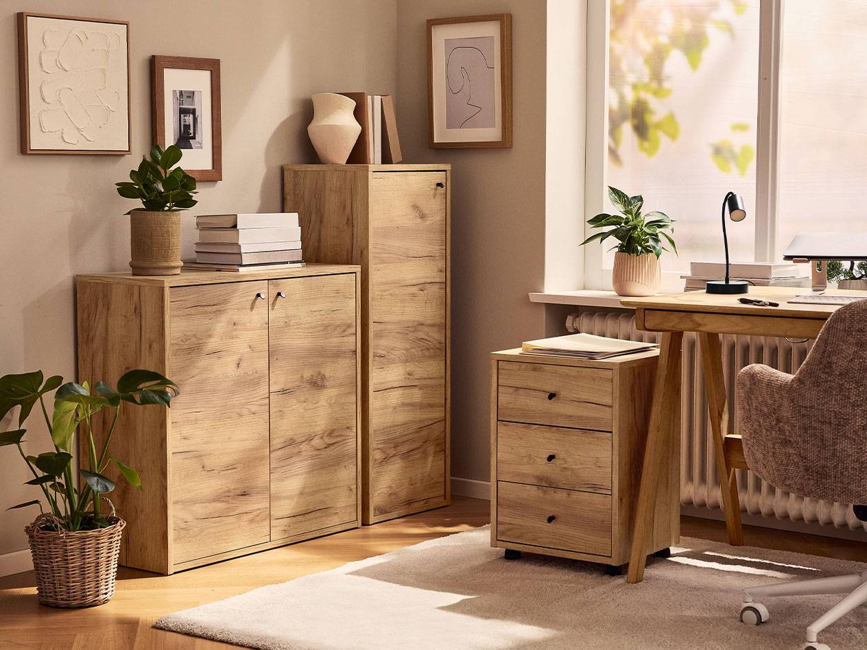 Domača pisarna s svetlimi lesenimi omarami, pisarniškim stolom in namizno svetilko.