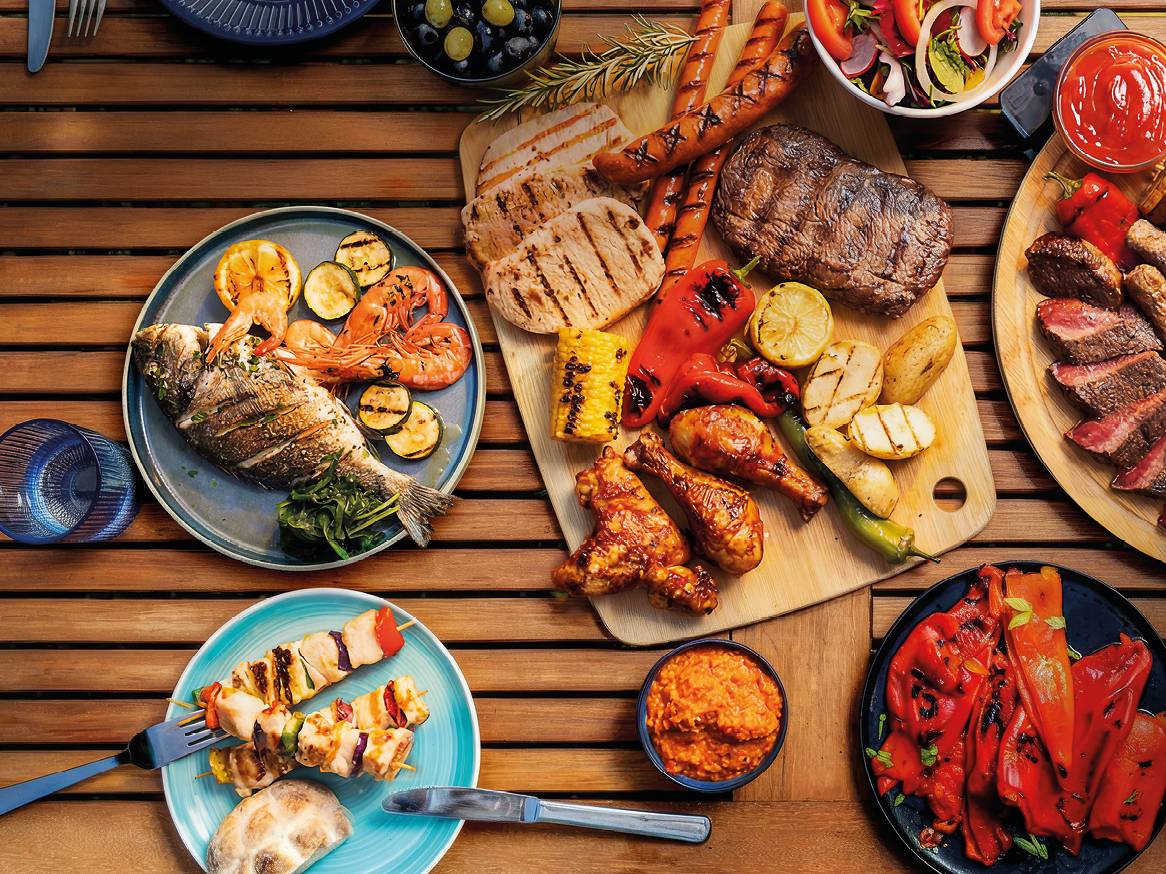Piknik miza s pestro izbiro mesa, rib, morskih sadežev in zelenjave na žaru.