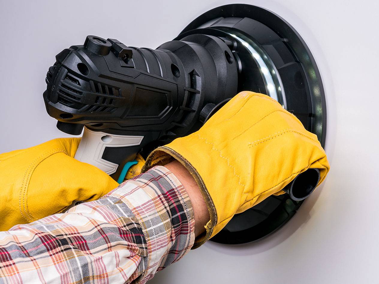 Električni stenski brusilnik z LED lučjo, ki ga uporablja oseba z rokavicami.
