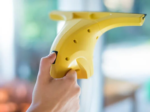 Roka drži rumen električni čistilec oken, čisti okno.