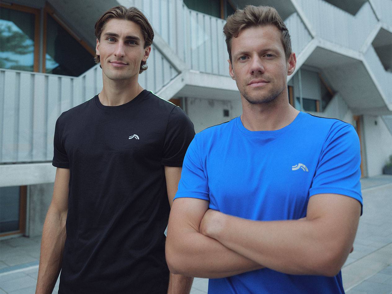 Dva moška v črnih in modrih športnih majicah z logotipom.