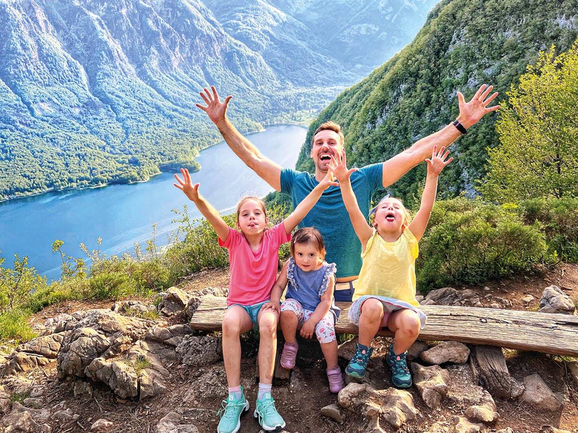 Očka z tremi hčerkami uživajo na izletu v gorah z razgledom na jezero.