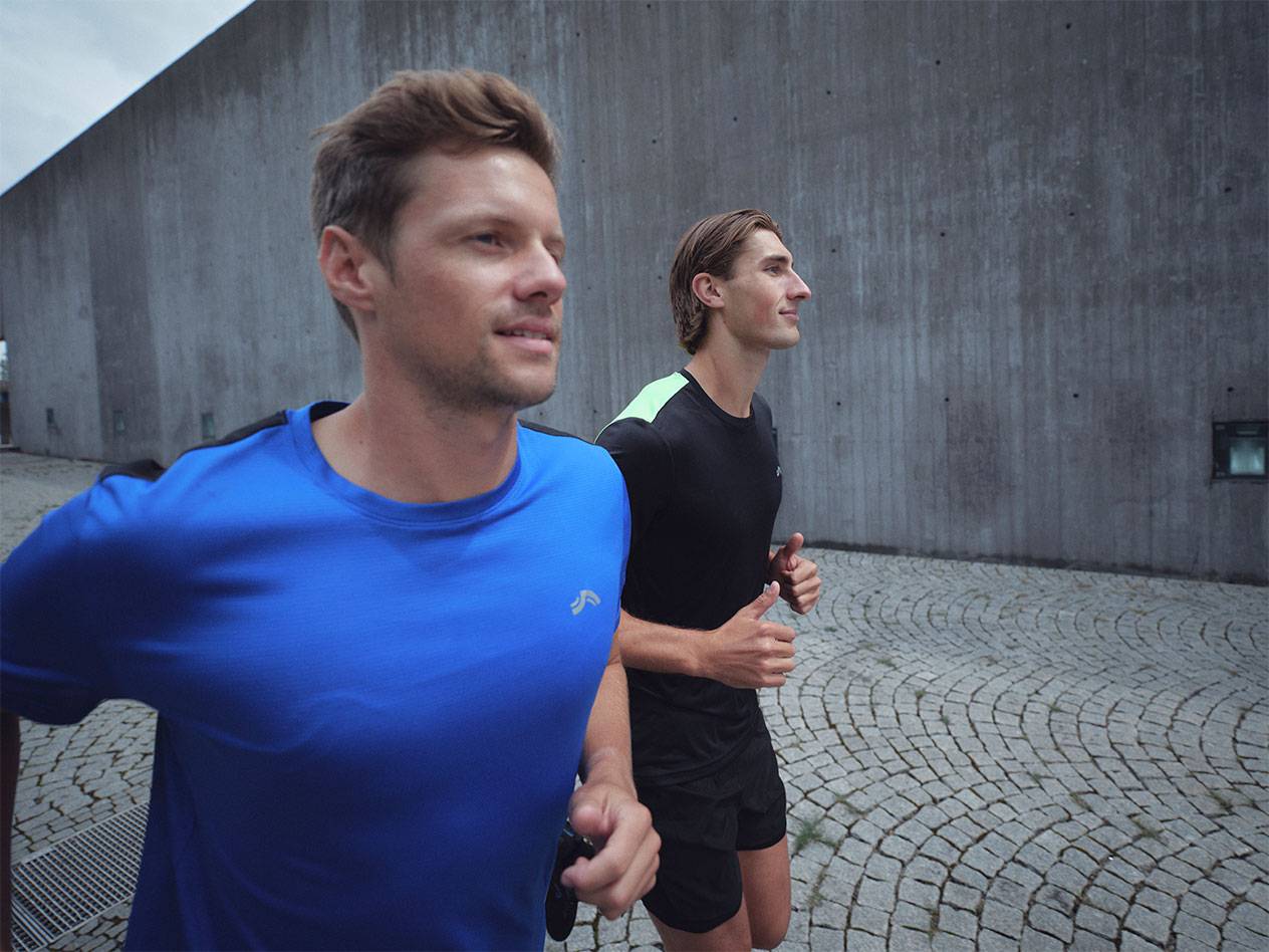 Dva moška tečeta v športnih majicah in kratkih hlačah, eden v modri, drugi v črni.