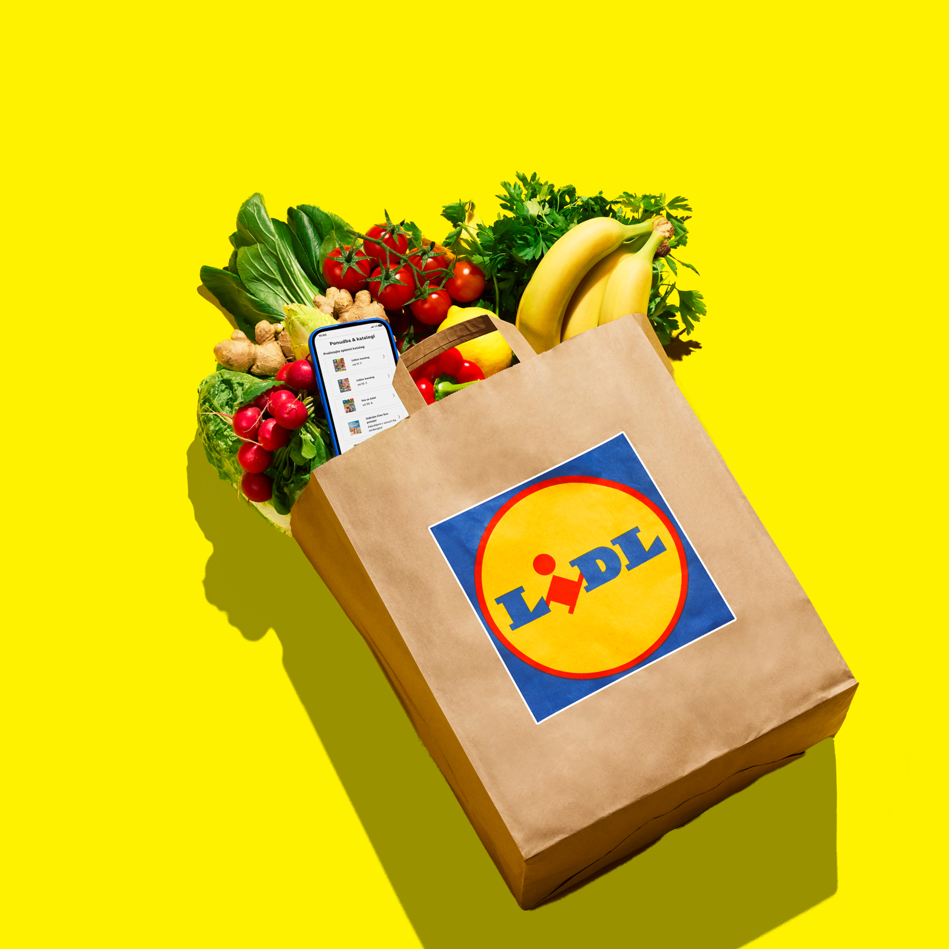 Papirnata nakupovalna vrečka, polna svežega sadja in zelenjave, z mobilno aplikacijo.