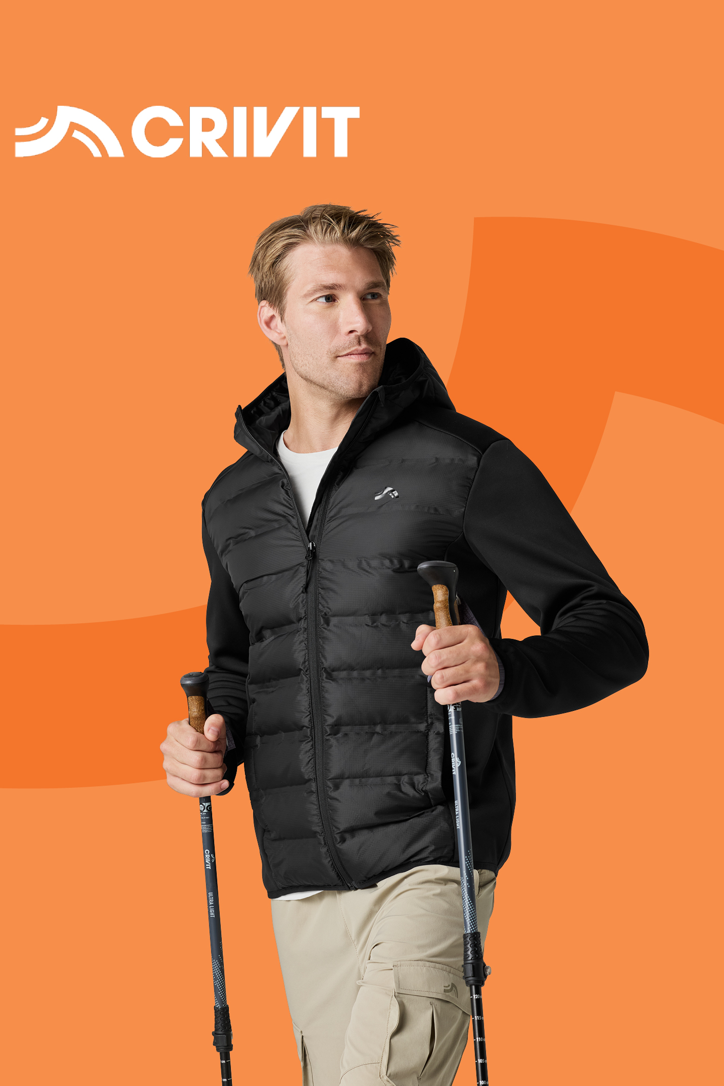 Moški v črni prešiti jakni in bež hlačah drži pohodniške palice.