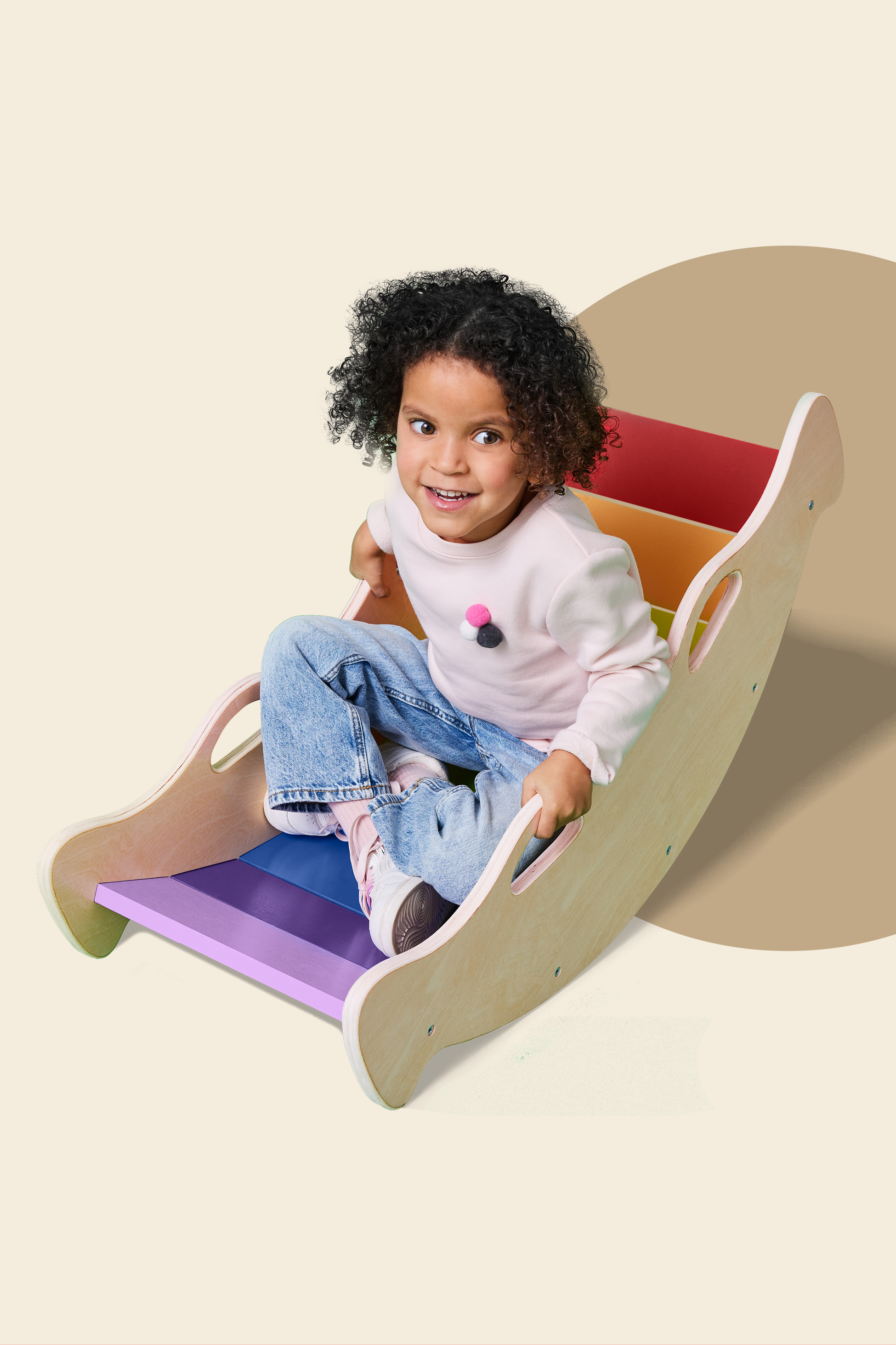 Deklica se igra na lesenem gugalniku mavričnih barv.