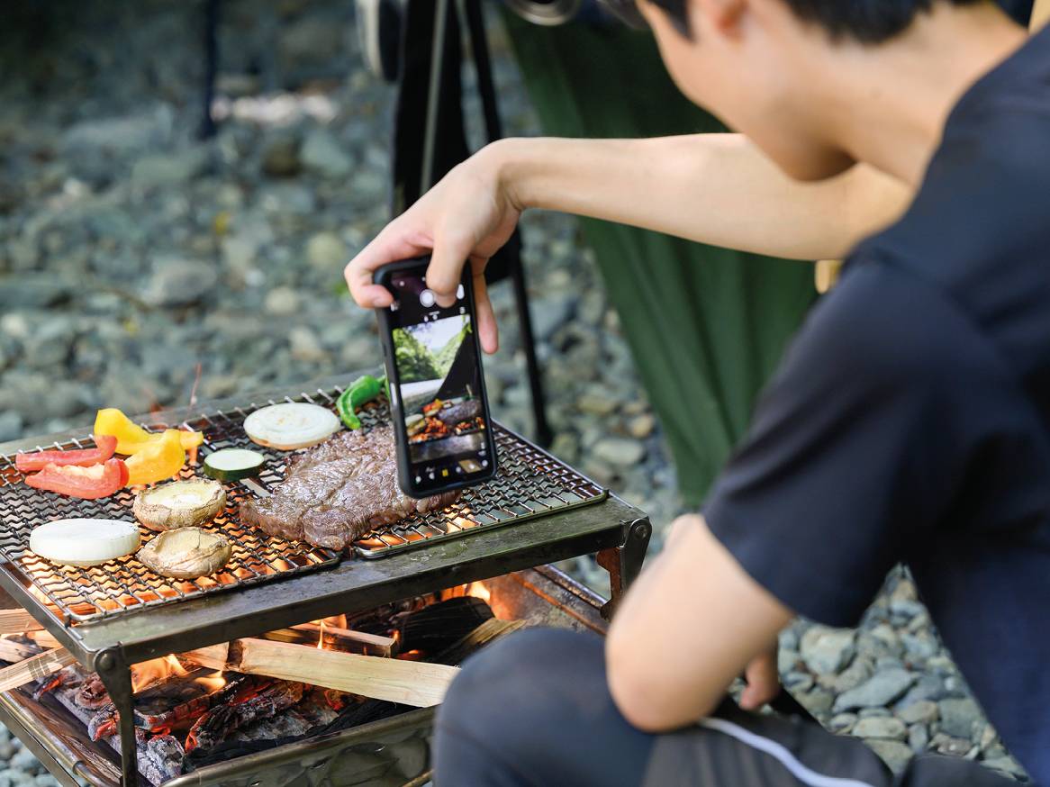 Moški fotografira žar z mesom in zelenjavo na prostem.