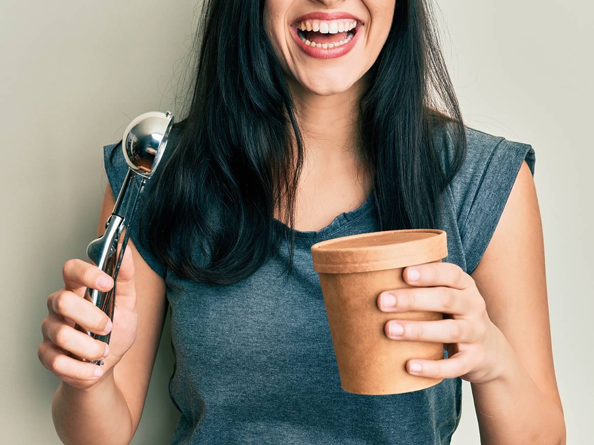 Nasmejana ženska drži zajemalko za sladoled in posodo za sladoled.