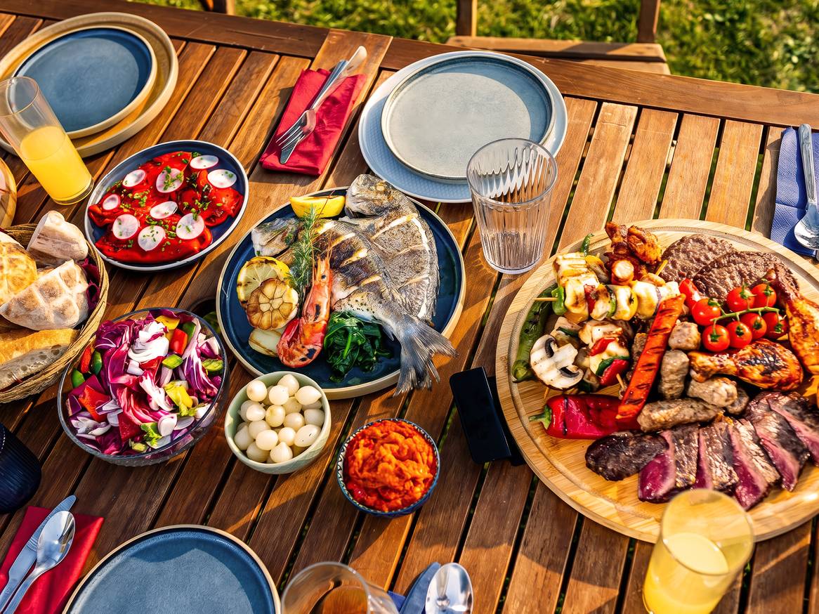 Piknik miza z žarom, ribami, solatami in pijačo na prostem.