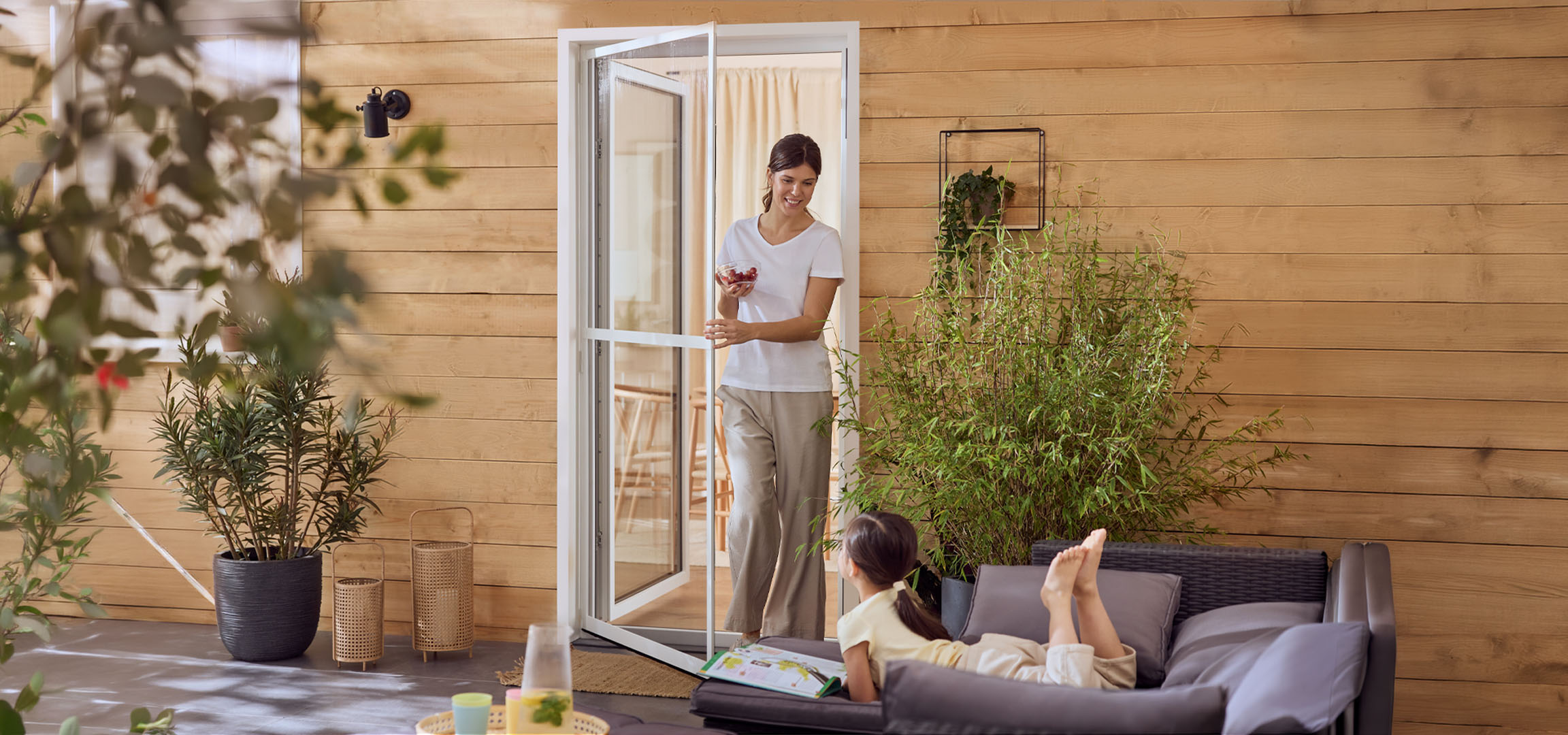 Ženska in deklica uživata na terasi z zunanjim pohištvom in rastlinami.