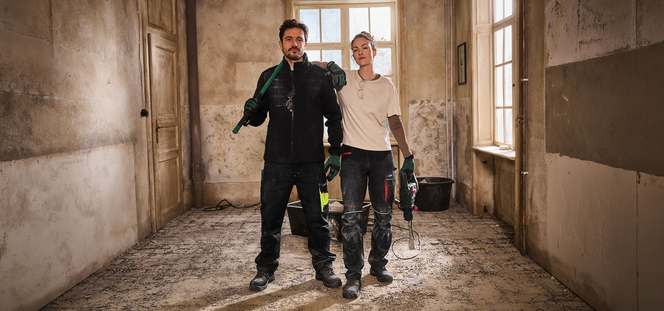 Dva gradbena delavca v delovni obleki z orodjem na gradbišču.