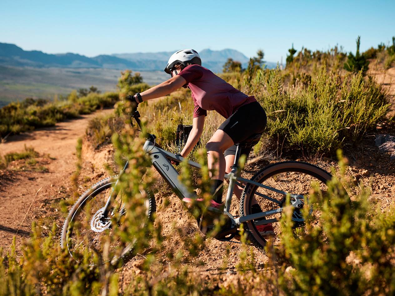 Ženska na gorskem kolesu na makadamski poti s pogledom na gore.