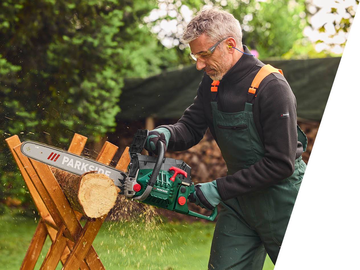 Moški v delovni obleki žaga deblo z motorno žago Parkside.