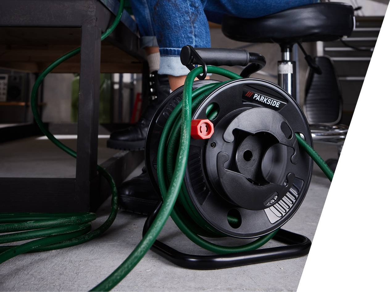 Parkside kolut za vrtno cev z navito zeleno cevjo na tleh.