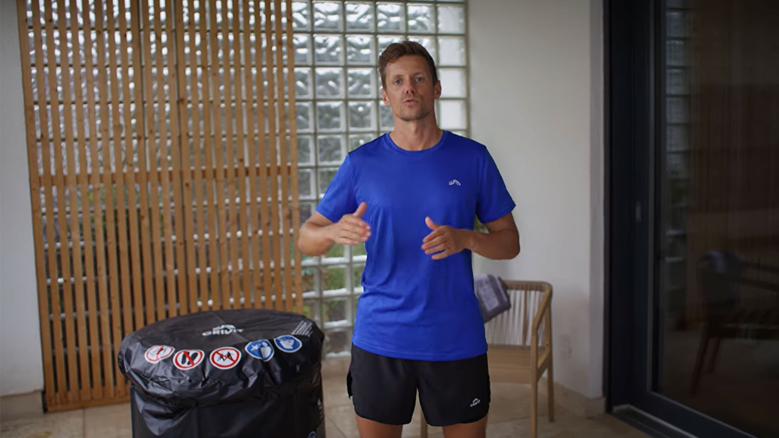 Moški v modri majici in črnih kratkih hlačah, poleg črnega pokrova za masažno kad.