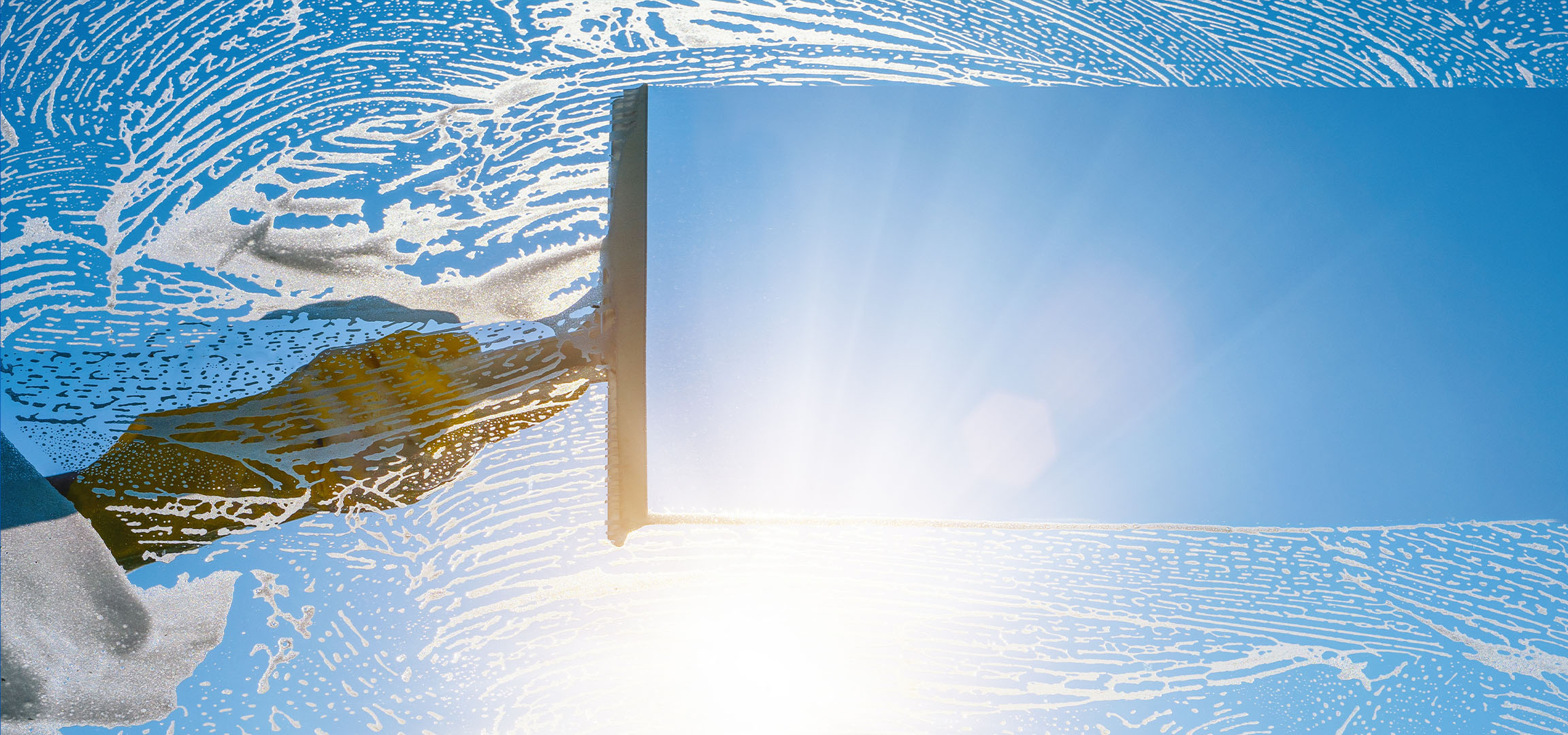 Čiščenje oken z milno peno na modrem nebu.